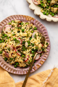 Orzo salad on pink plate with gold fork on marble background