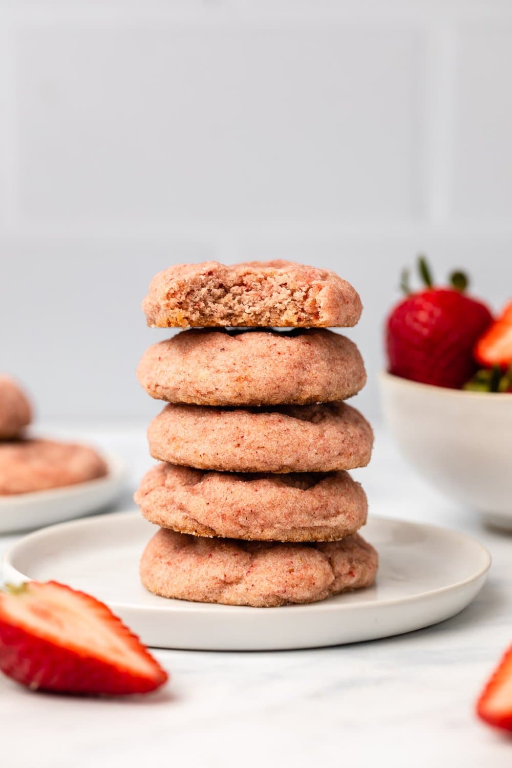 Stack of strawberry sugar cookies on white plate with bowl of strawberries in the background