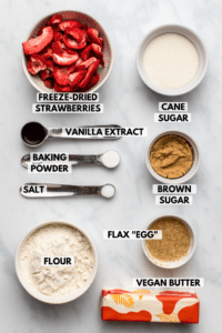 Ingredients for strawberry sugar cookies in white bowls on marble countertop