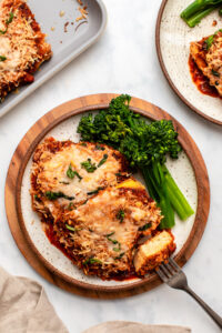 tofu parmesan on plate with steamed broccolini and bite taken out of it