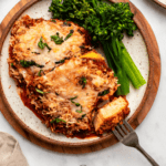 tofu parmesan on plate with steamed broccolini and bite taken out of it