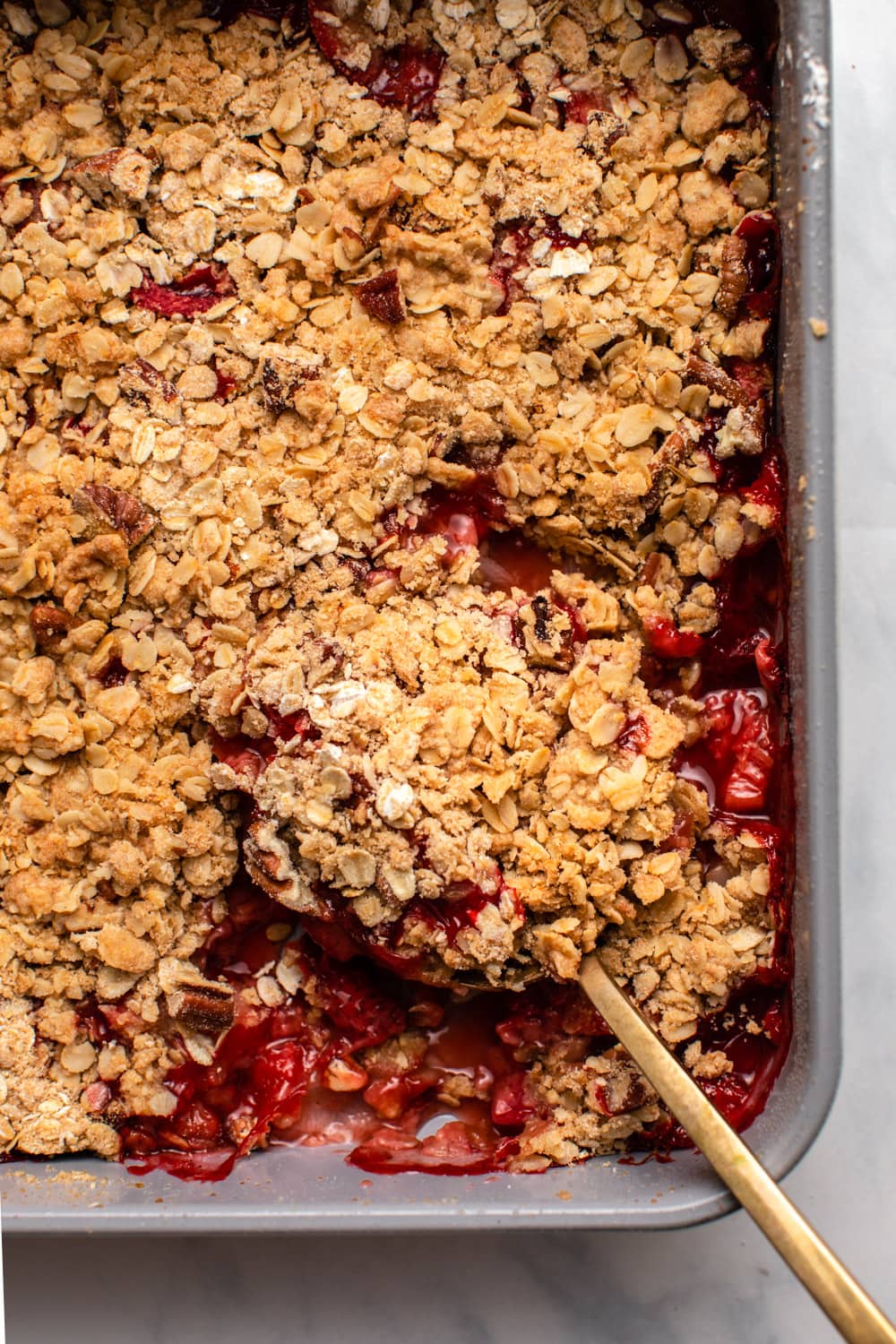 Baked strawberry rhubarb crisp with spoon taking scoop of it out