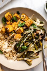 roasted veggies and crispy tofu in bowl with rice, topped with tahini sauce