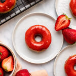 strawberry donuts on small white plates with fresh cut strawberries on the side