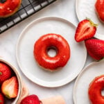 strawberry donuts on small white plates with fresh cut strawberries on the side