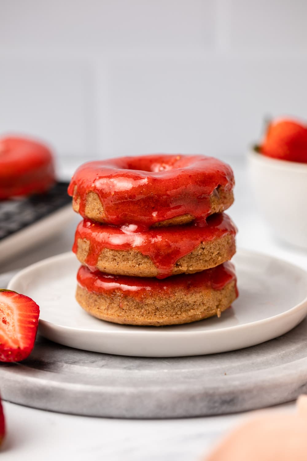 stack of glazed strawberry donuts with bowl of strawberries in the background