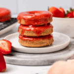 stack of glazed strawberry donuts with bowl of strawberries in the background