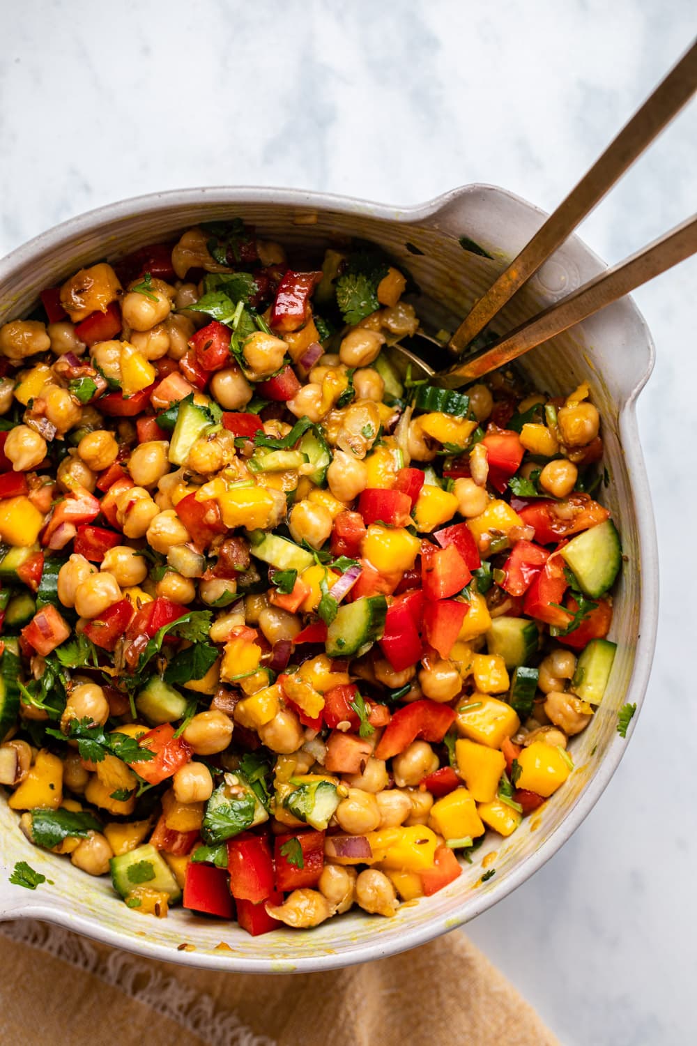 Mango and chickpea salad in white serving bowl with gold tongs