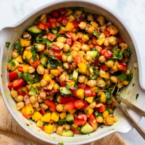 Mango chickpea salad in large white bowl with golden utensils