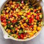 Mango chickpea salad in large white bowl with golden utensils