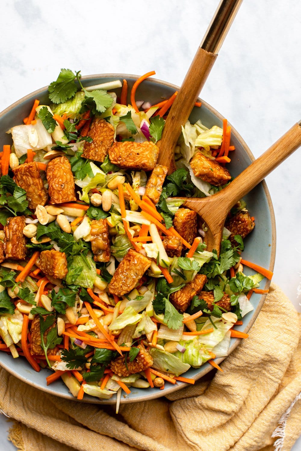 tempeh salad in large bowl with wooden serving spoons on marble countertop