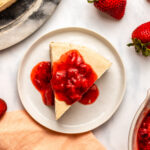 slice of cheesecake topped with strawberry compote on white plate
