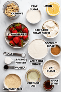 Ingredients for vegan strawberry cheesecake in small bowls on marble background