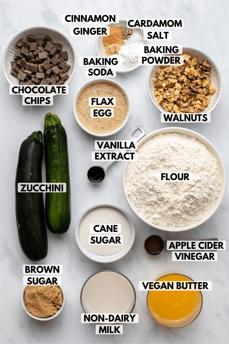 Ingredients for zucchini muffins in small white bowls on marble background