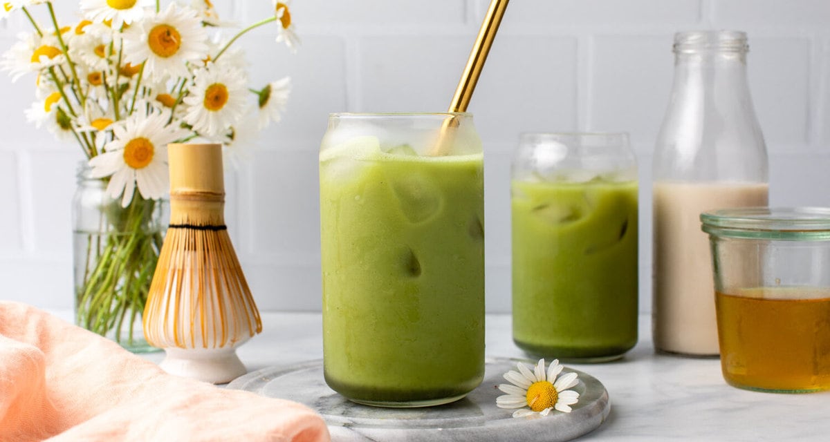 Two glasses of matcha latte with ice and gold straw