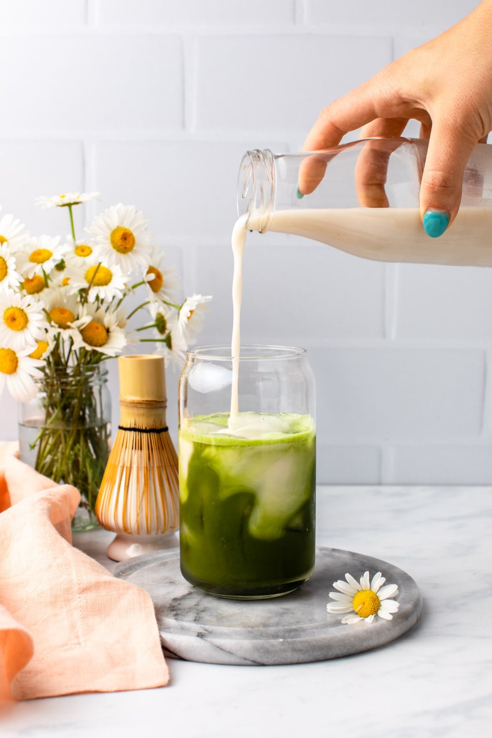 hand pouring milk over chamomile and matcha mixture in glass with ice