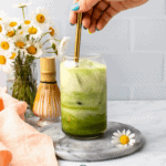 hand stirring plant milk into matcha and chamomile drink in glass with ice