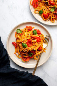 spicy tomato basil pasta on two white plates with gold forks