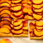 puff pastry peach galette sliced and resting on tan parchment paper