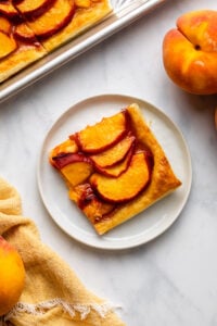 slice of puff pastry peach galette on white plate on marble background