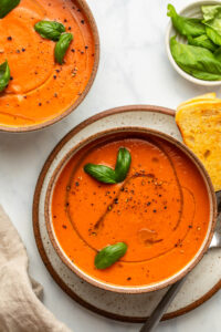 two bowls of tomato soup topped with olive oil and fresh basil