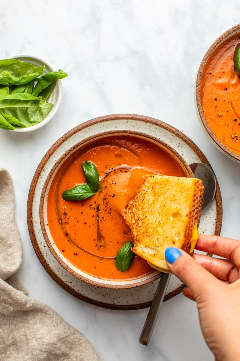 hand dunking grilled cheese into bowl of tomato soup
