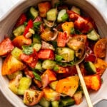 Tomato and cucumber salad in large serving bowl with golden spoon