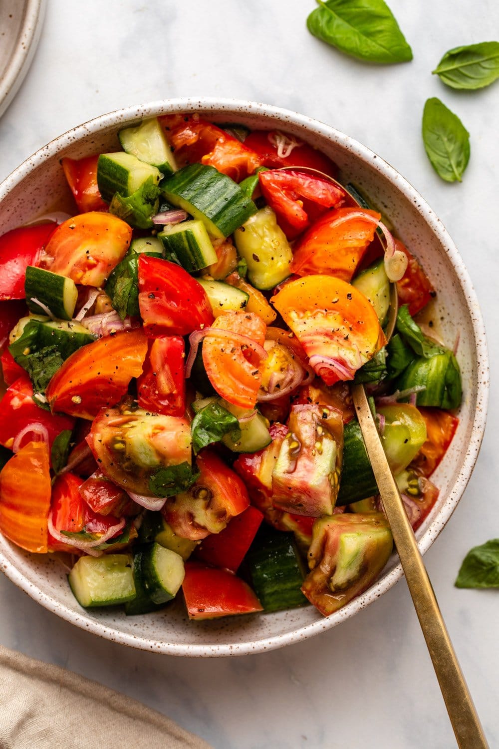 Tomato and cucumber salad in serving bowl with fresh basil