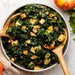 kale apple walnut salad in large white bowl with wooden serving tongs