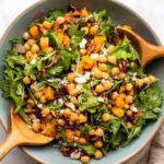 roasted butternut squash salad with pecans and vegan feta in large serving bowl with wooden serving spoons