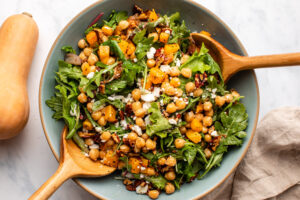 roasted butternut squash salad with pecans and vegan feta in large serving bowl with wooden serving spoons