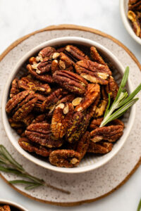 bowl of roasted rosemary pecans with fresh rosemary