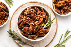 roasted rosemary pecans in small bowl with fresh rosemary