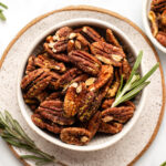 roasted rosemary pecans in small bowl with fresh rosemary