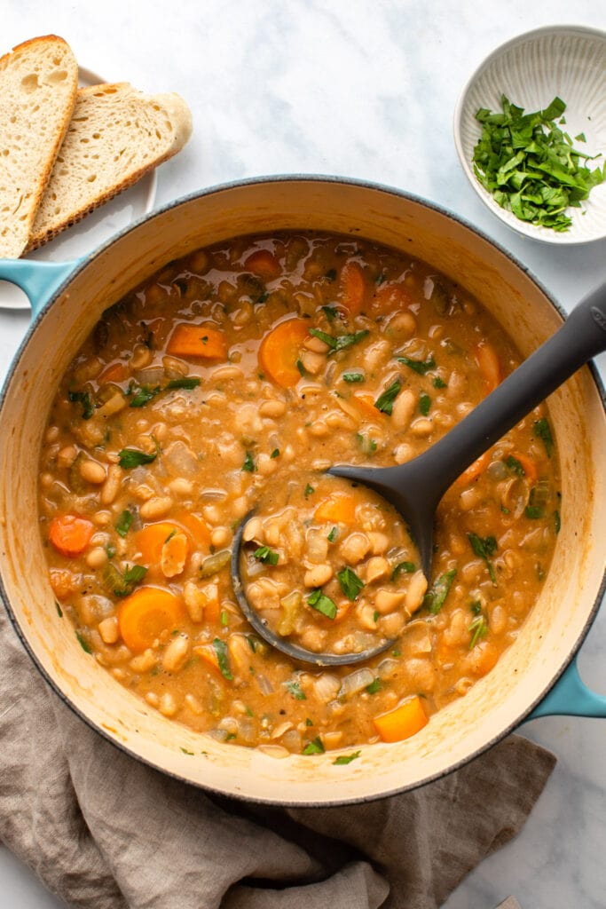 white bean stew in dutch oven with bread and parsley on the side
