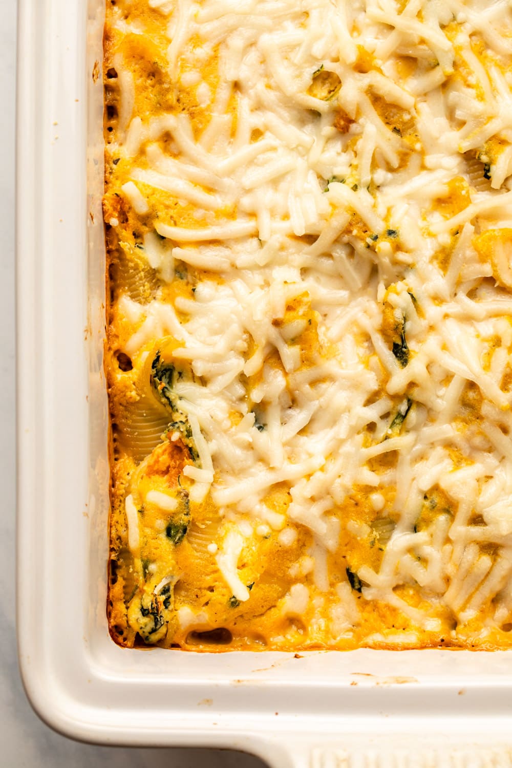 butternut squash shells topped with vegan cheese in baking dish