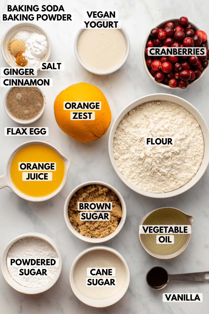 Ingredients for cranberry orange muffins in small bowls on marble countertop