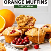 three vegan cranberry orange muffins stacked on top of a baking tray with several cranberries spread around