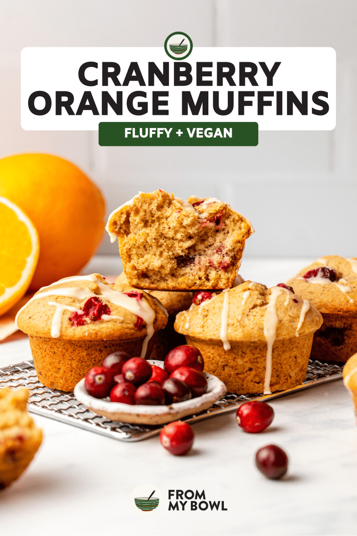three vegan cranberry orange muffins stacked on top of a baking tray with several cranberries spread around