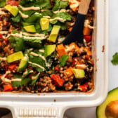Chipotle black bean casserole topped with avocado and cilantro with serving spoon in casserole dish