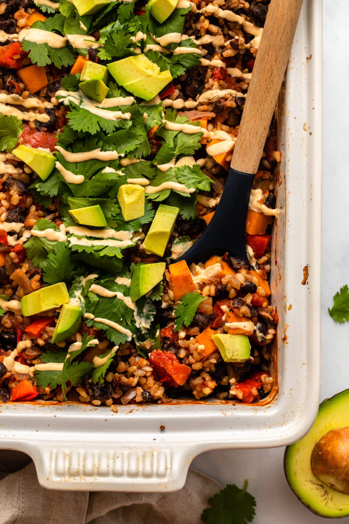 a spoon scooping up chipotle black bean casserole on a stovetop with cilantro and an avocado on the side