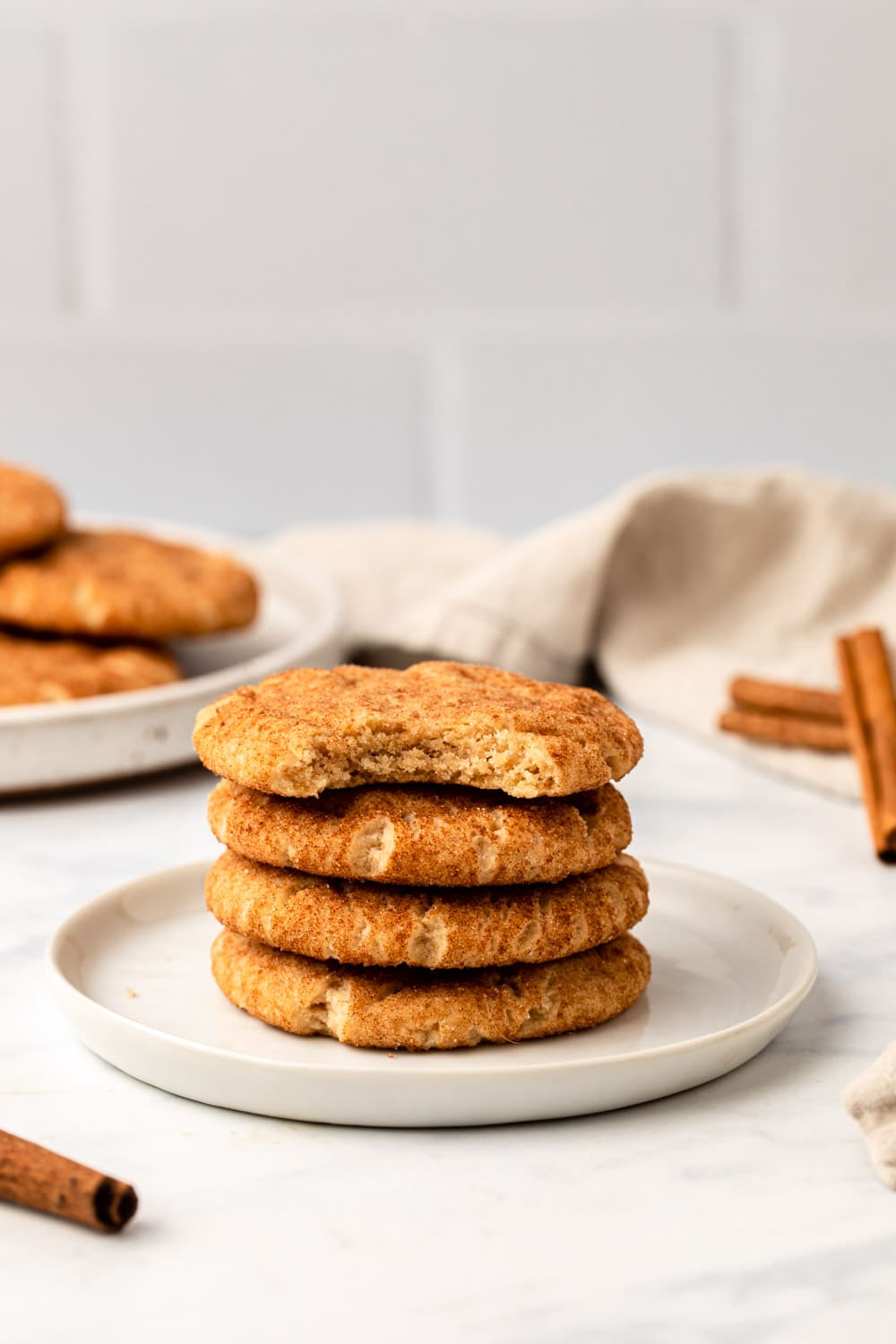 four vegan snickerdoodles stacked on a white serving plate, with one bite taken off the cookie on top