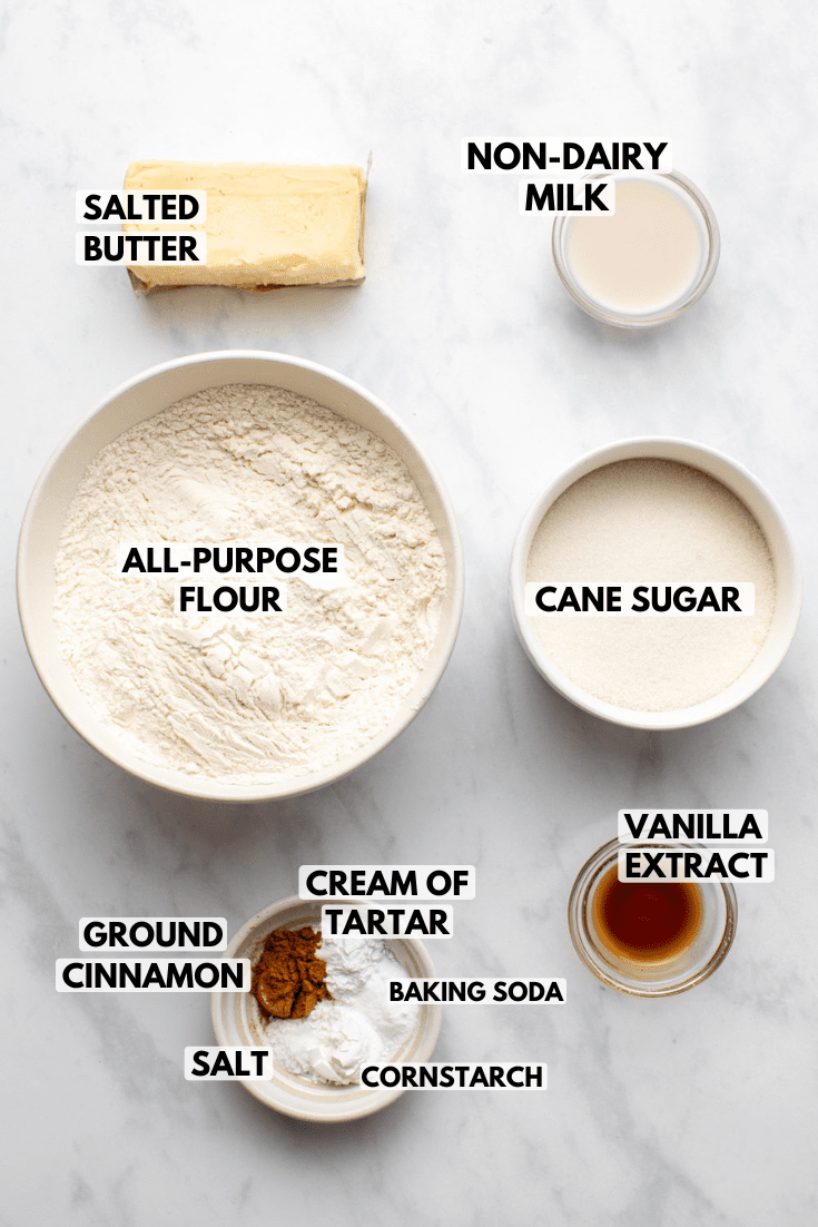 ingredients for vegan snickerdoodles served in white bowls and laid out on a marble kitchen counter