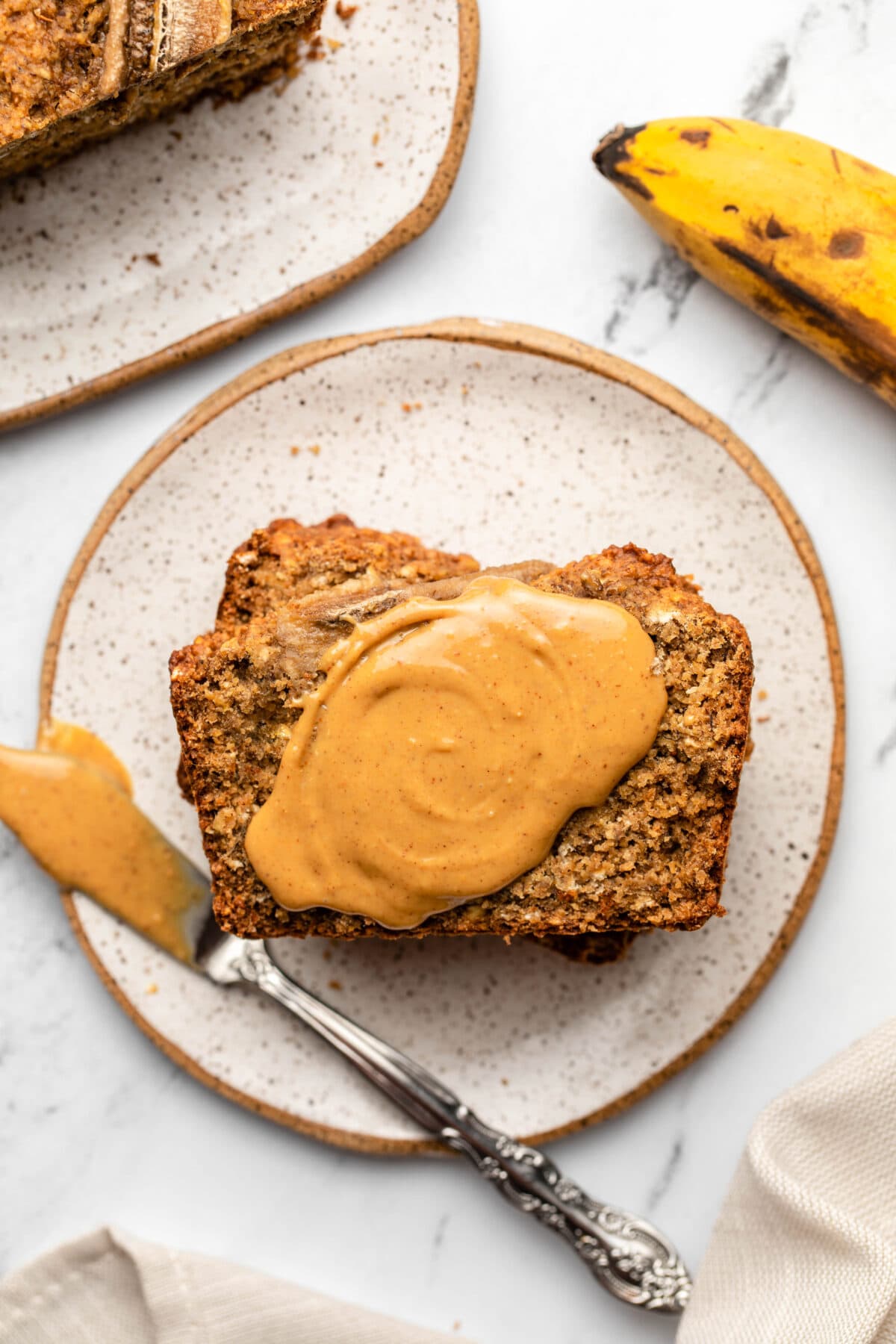 three servings of the banana bread stacked, topped with nut butter with the butter knife displayed next to the banana bread slices