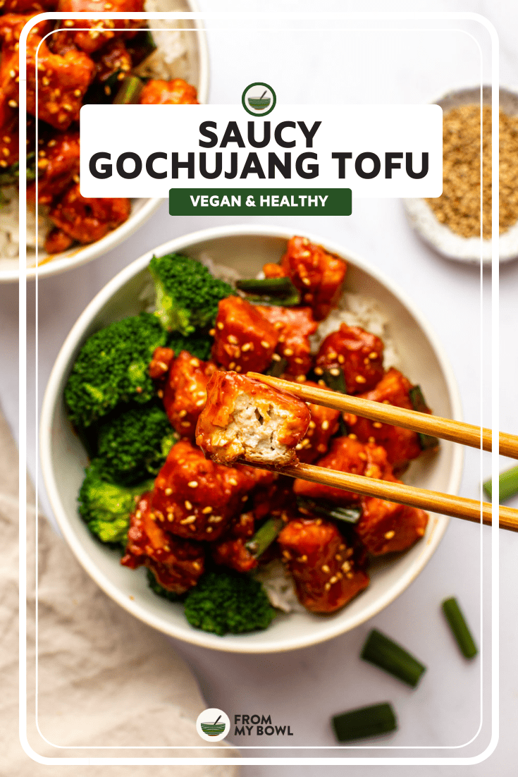 chopsticks holding piece of tofu over bowl of gochujang tofu