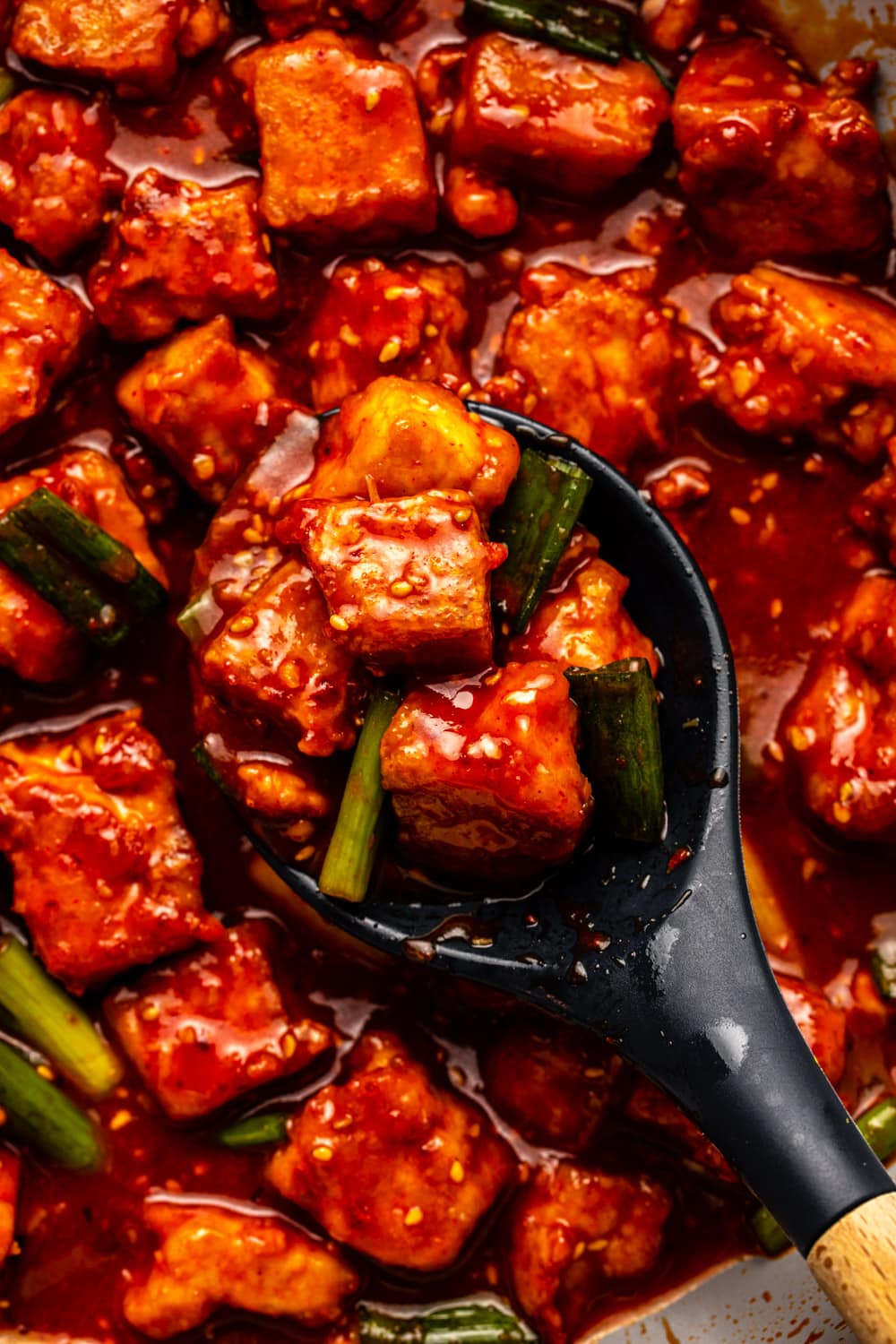 a zoomed in image of a serving spoon scooping up gochujang tofu from the pan