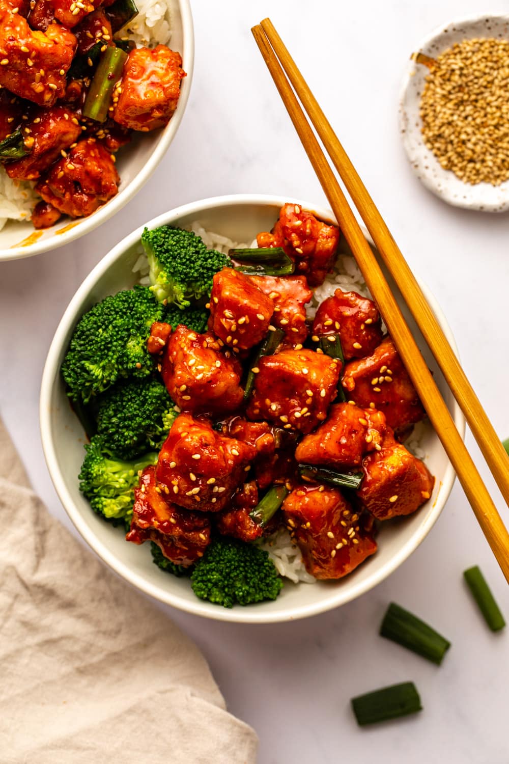 saucy gochujang tofu served with broccoli and rice in a white bowl with chopsticks on the bowl for presentation purposes