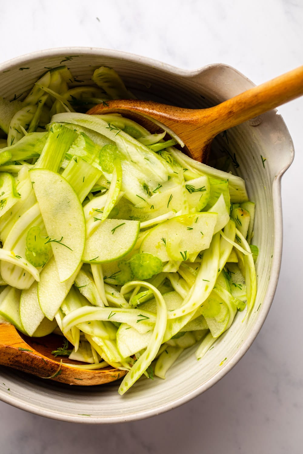 shaved fennel salad served in a white bowl with two serving spoons mixing it