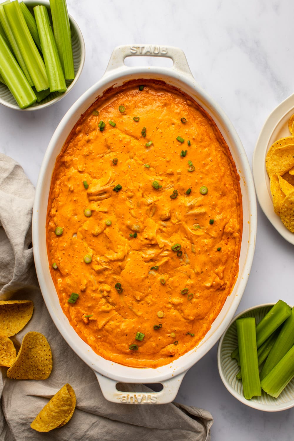 vegan buffalo chicken dip freshly out of the oven in a baking dish served on a kitchen countertop, served with tortilla chips and celery