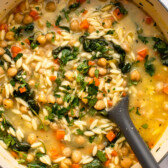 Large pot of lemon chickpea orzo soup with soup spoon mixing the soup
